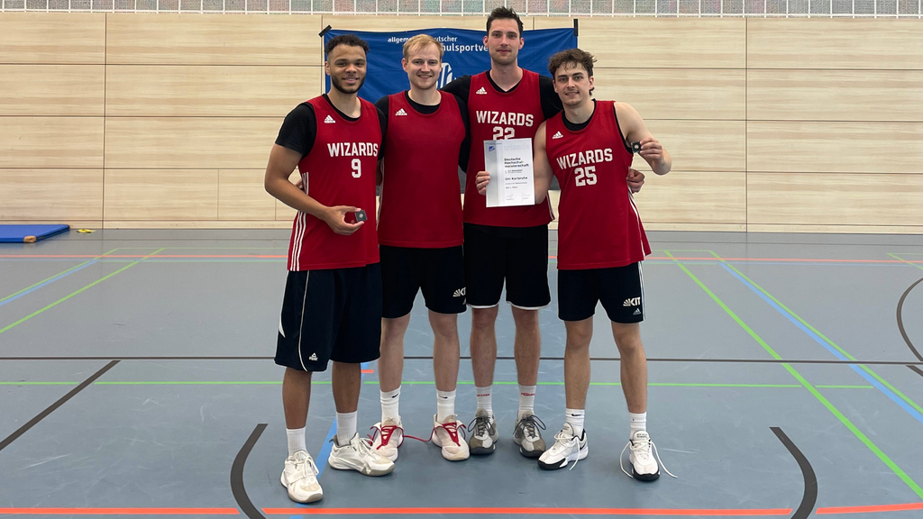 Vier Basketballspieler im roten Trikot posieren mit einer Urkunde in der Sporthalle.