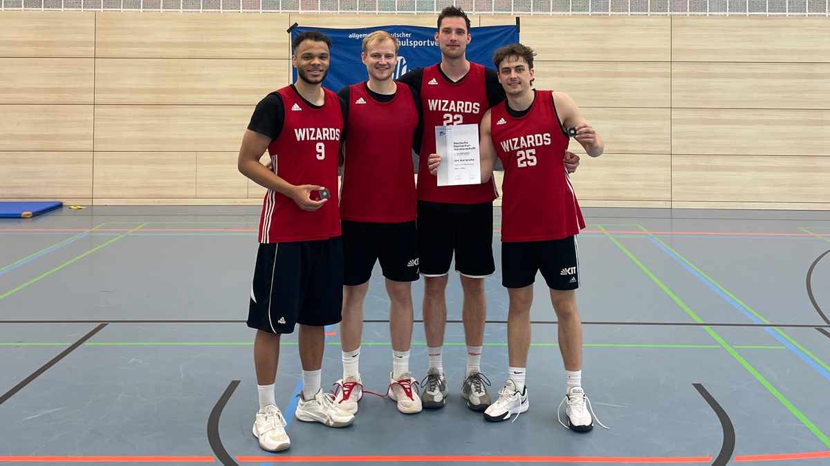 Vier Basketballspieler in roter Kleidung stehen in einer Sporthalle und halten eine Urkunde.