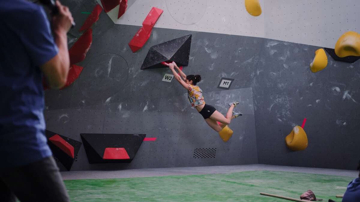 Person beim Bouldern in einer Indoor-Kletterhalle, springt zu Wand an Rot-Gelb-Griffen.