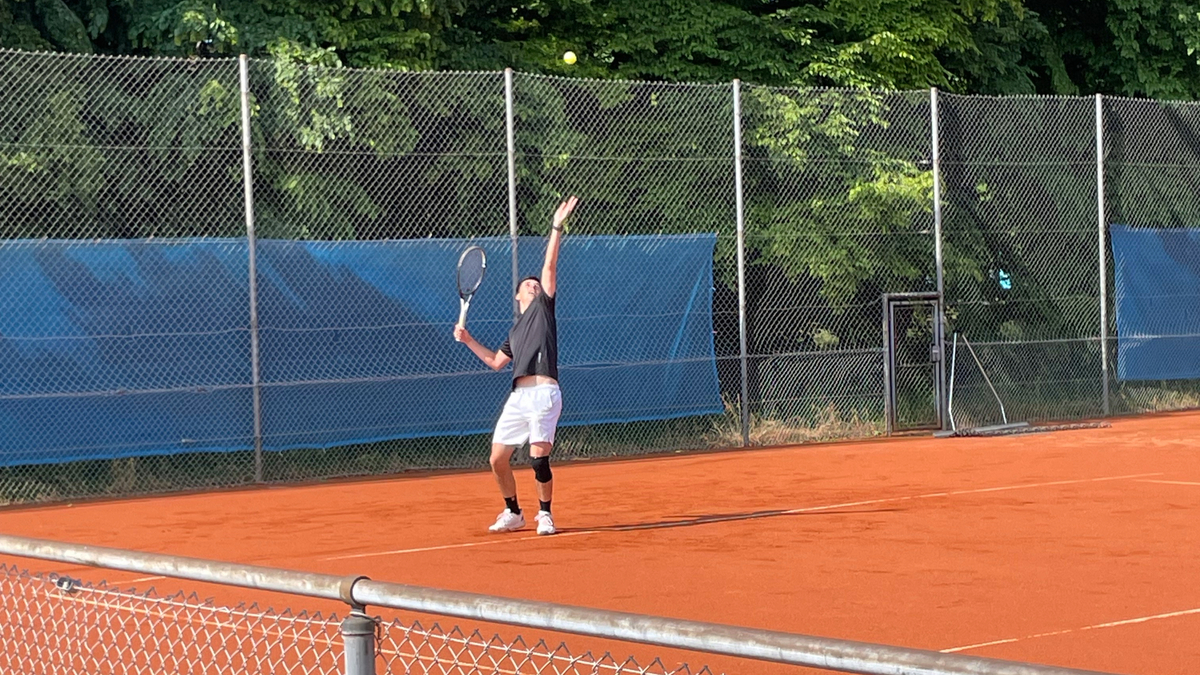 Tennisspieler beim Aufschlag auf rotem Sandplatz.