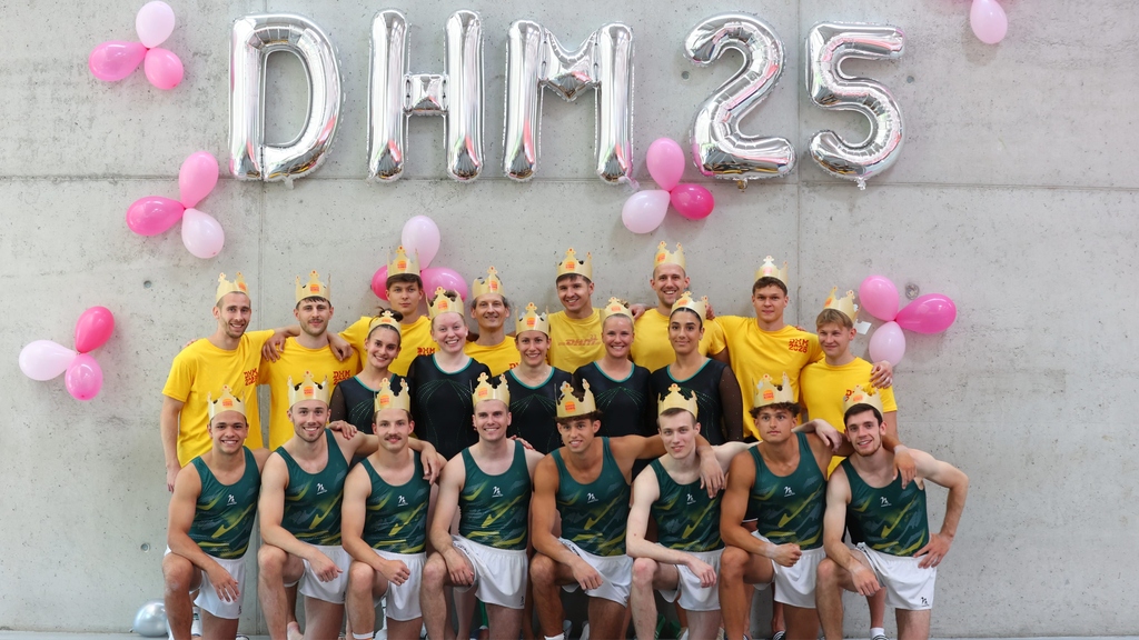 Gruppe mit gelben T-Shirts und Kronen vor Ballondekoration "DHM 25".
