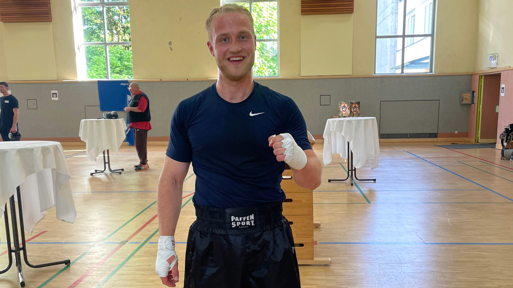 Ein Boxsportler lächelt in einer Turnhalle, mit Bandagen an den Händen.