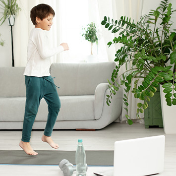 Junge macht zu Hause ein Online-Workout mit Laptop, Wasserflasche und Hantel.