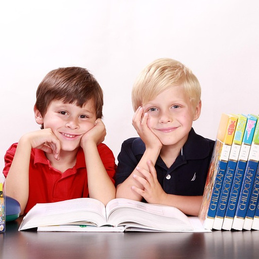 Zwei Kinder sitzen lächelnd am Tisch mit offenen Büchern und Enzyklopädien.